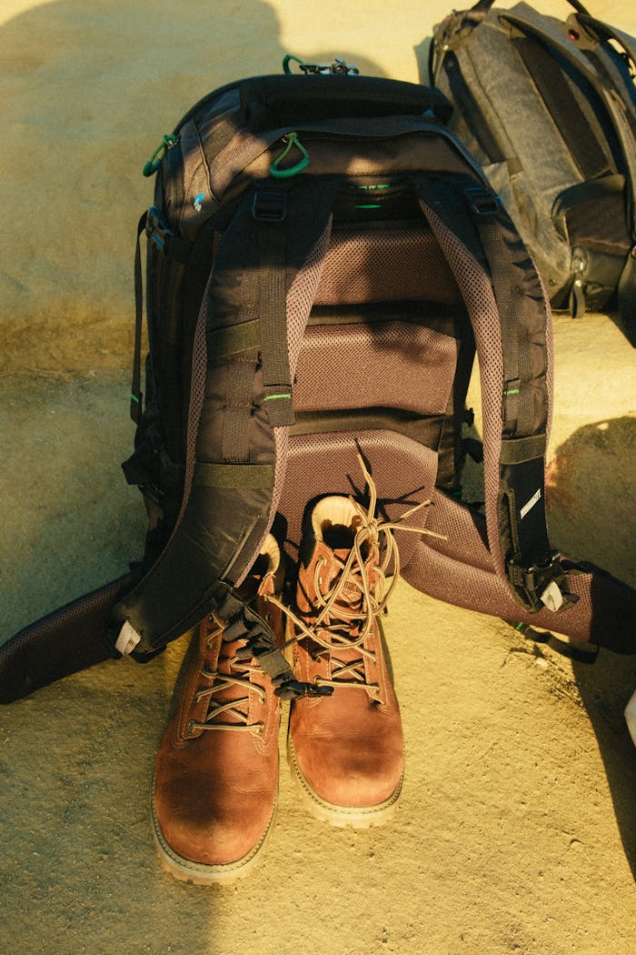 A backpack and boots arranged on a sandy surface, perfect for travel or adventure themes.