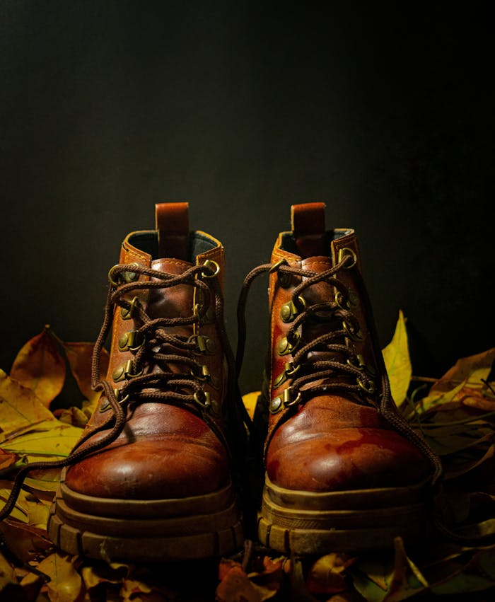 Pair of rugged brown leather boots surrounded by fallen autumn leaves.