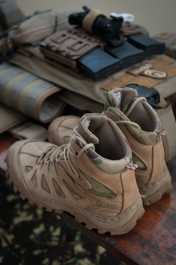 Close-up of tactical hiking boots with outdoor gear arranged on a wooden surface.